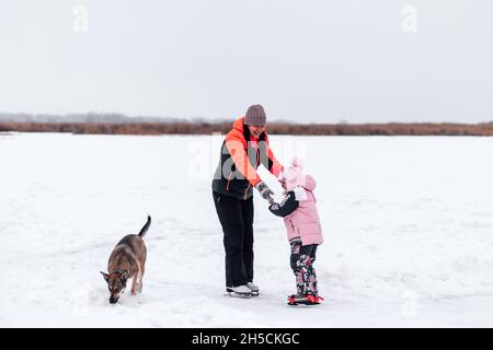 Maman et fille sur la promenade d'hiver.Une jeune femme et une petite fille marchent le long de la berge gelée, des jeux de chien à côté d'eux, paysage d'hiver Banque D'Images