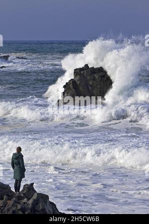 Femme se tient sur la côte de lave noire et regardant le surf de l'océan torrencieux , Islande, Snaefellsnes, Skardsvik Banque D'Images