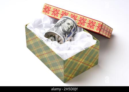 Une boîte cadeau sur le thème des fêtes avec un rouleau de billets de cent dollars. Banque D'Images