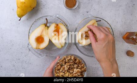 Poires cuites aux noix, au miel et à la cannelle, gros plan sur un fond rustique, petit déjeuner ou dessert parfait, plat, mains de femme Banque D'Images