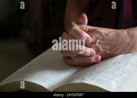 Vue rapprochée de la femme âgée mains sur la bible ouverte, pliée dans la prière. Banque D'Images