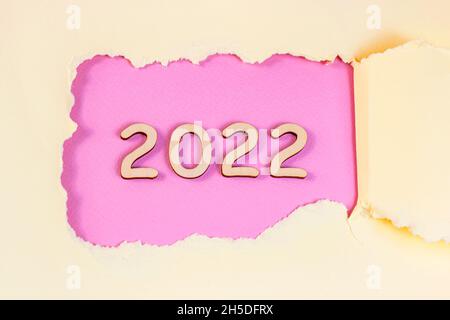 Silhouette en bois numéros 2022 avec trou de papier rose déchiré rugueux sur fond clair.Félicitations et concept de planification pour le début de la nouvelle année. Banque D'Images