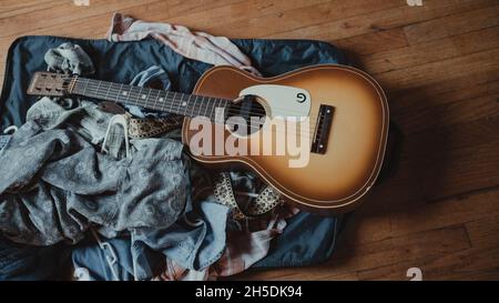 Guitare reposant sur une pile de jeans et de vestes bleus Banque D'Images