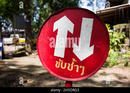 Entourez le panneau rouge avec deux directions et la langue thaï signifie conduire lentement sur une petite voie dans la région. Banque D'Images