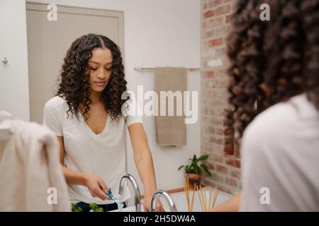 Miroir réflexion d'une jeune femme afro-américaine sur le point de se brosser les dents avec Une brosse à dents dans la salle de bains Banque D'Images