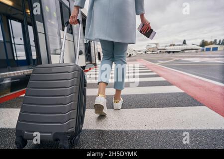 Passager élégant avec valise à roulettes approchant le véhicule de transport Banque D'Images