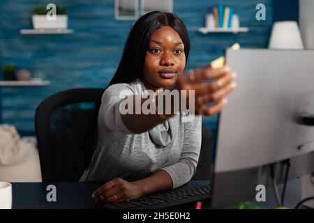 Adulte mettant des notes adhésives sur le moniteur pour travailler à distance.Jeune personne utilisant le papier posttit sur ordinateur pour aider avec le projet d'affaires tout en travaillant à la maison.Femme avec note adhésive Banque D'Images