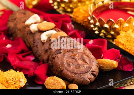 Assortiment de desserts indiens doux Thokwa Thekua ou Thekuwa décoré de fruits secs dans un plateau noir avec des fleurs tout autour pendant Chhath Puja Holi Celebra Banque D'Images