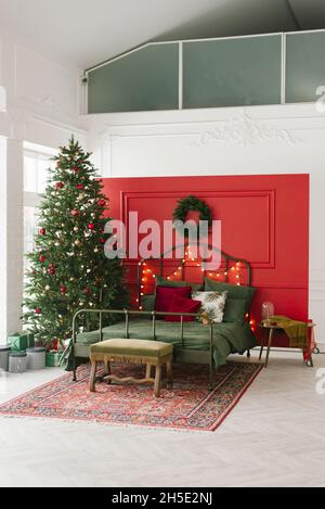 Une chambre classique avec un sapin de Noël et des décorations traditionnelles rouges et vertes.Lit sur le fond du mur près de la fenêtre Banque D'Images