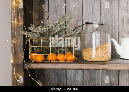 Un panier avec des mandarines et des branches de sapin est sur une étagère avec des ustensiles de cuisine.Décoration de Noël Banque D'Images