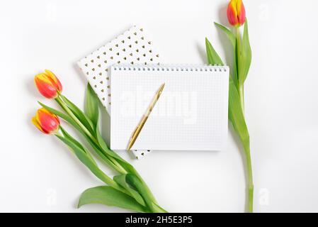 Bloc-notes en spirale ouvert avec stylo et tulipes rouges sur fond de bureau blanc.Modèle pour la publicité ou la visualisation de blog avec espace de copie pour le texte.Busi Banque D'Images