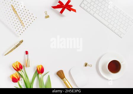 Carte postale pour la Saint-Valentin, la fête des mères ou le 8 mars.Un bouquet de tulipes, un cadeau avec un noeud rouge, une tasse de thé, des cosmétiques et un carnet avec un stylo. Banque D'Images