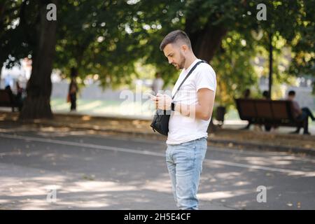 Homme en t-shirt blanc avec sac de fer noir utilisant le téléphone outddorr.L'homme a la montre intelligente Banque D'Images