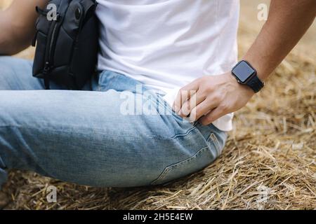 Gros plan de l'homme s'assoit sur un banc de foin et prend le téléphone de sa poche Banque D'Images