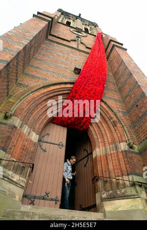 Cradley, West Midlands, Royaume-Uni.9 novembre 2021.Le gardien de l'église Paul Millward déverrouille les portes de l'église paroissiale de Saint-Pierre à Cradley, dans les West Midlands, tandis qu'une cascade de 75 mètres de coquelicots en maille orne la tour de l'église avant le dimanche du souvenir.Des milliers de coquelicots tricotés à la main ont été créés par les habitants de la région ainsi que par des contributeurs à l'étranger, et ont été l'enfant de Doreen Clifton, un résident de la région.Crédit : Peter Lophan/Alay Live News Banque D'Images