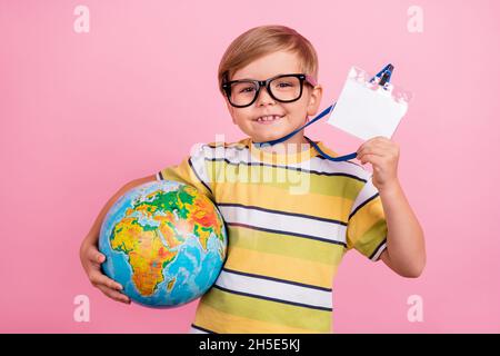 Photo de jeune heureux positif petit garçon tenir main ID tag globe pupille sourire isolé sur fond de couleur rose Banque D'Images