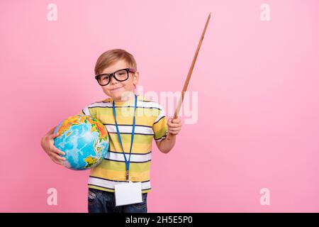 Photo de jeune petit garçon heureux tenir main pointeur bâton de leçon de globe isolé sur fond de couleur rose Banque D'Images