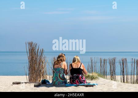 Vue à angle bas de deux femmes vues sur leur dos dans une robe colorée assise sur la plage de l'île de Texel, les pays-Bas donnant sur une mer bleue calme surr Banque D'Images