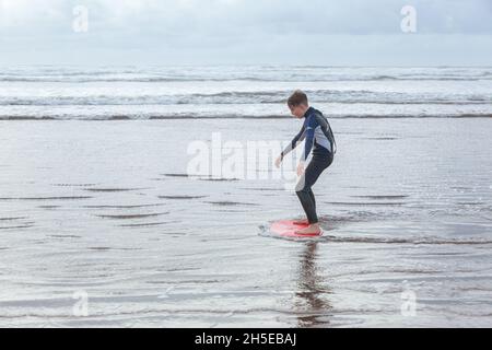 Skimboarding de garçon de douze ans à Westward Ho !beach, Devon, Angleterre, Royaume-Uni Banque D'Images