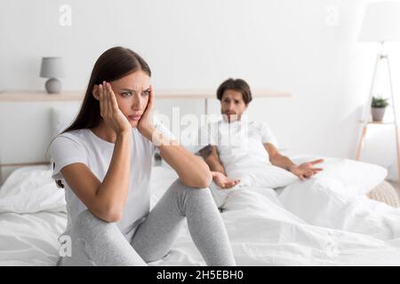 Triste mécontent mari du millénaire caucasien avec un chaume est assis sur le lit criant à la femme offended Banque D'Images