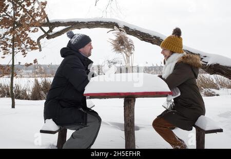 homme et femme heureux dans l'amour, mari et femme dans des vêtements chauds d'hiver, assis sur des bancs dans un parc d'hiver face à l'autre, promenades d'hiver Banque D'Images