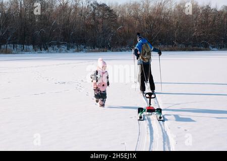 Promenade en famille en forêt en hiver.Un jeune homme et un enfant marchent dans la nature, une fille court près de son père, qui skine et conduit des enfants en traîneau Banque D'Images