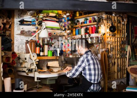 homme travailleur couture de points sur la ceinture dans un atelier de cuir Banque D'Images