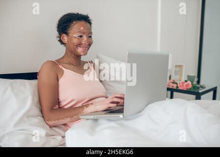 Une femme assise au lit et travaillant sur un ordinateur portable Banque D'Images