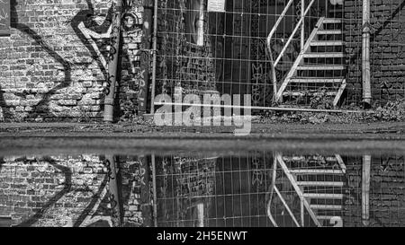 photo de rue d'un mur de graffiti et d'une clôture de construction reflétée dans une flaque, beaucoup de texture et rétro en noir et blanc Banque D'Images