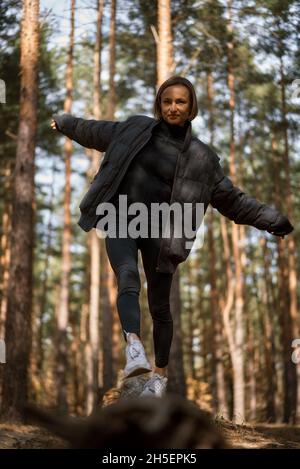 Une fille marche sur une bûche dans une forêt de pins en automne.Fille équilibrant sur une bûche dans la forêt Banque D'Images