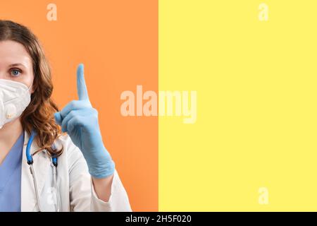 Le médecin fait un doigt prudent - mouvement vers le haut, espace de copie.Une femme en gants de protection médicale et un masque sur fond rouge, concept Banque D'Images