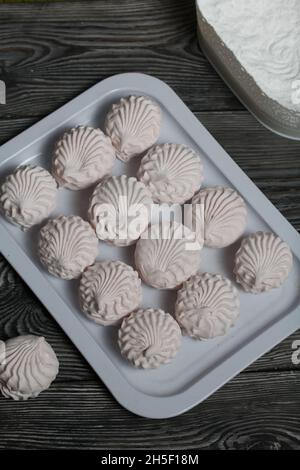 Marshmallows faits maison sur un plateau Zephyr en poudre de sucre, allongé en rangées.Sur la surface des planches de pin noir. Banque D'Images