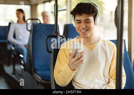 Joyeux homme asiatique souriant écoutant de la musique dans le bus Banque D'Images