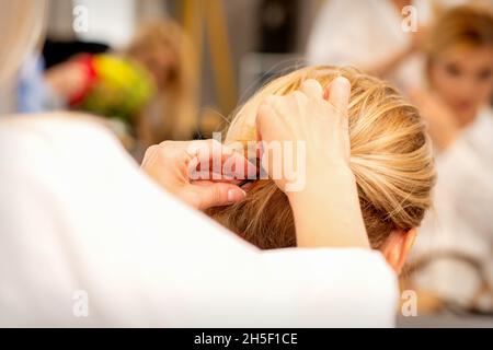 Mains de styliste de cheveux faisant la coiffure professionnelle des cheveux longs de femme dans un salon de beauté Banque D'Images