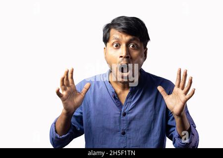 Un jeune indien en robe bleue avec un look choqué surpris et la bouche ouverte sur fond blanc Banque D'Images