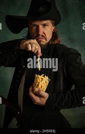 Portrait d'un homme brutal, pirate médéival tenant des frites isolées sur fond sombre. Banque D'Images