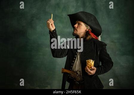 Portrait d'un homme brutal, pirate médéival tenant des frites isolées sur fond sombre. Banque D'Images