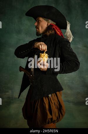 Portrait d'un homme brutal, pirate médéival tenant des frites isolées sur fond sombre. Banque D'Images