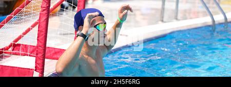 Un jeune homme se tient à la porte de la piscine et joue au water-polo à proximité Banque D'Images