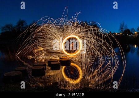 Peinture légère avec laine d'acier; exposition pyrotechnique la nuit avec réflexion dans l'eau. Banque D'Images