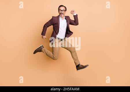 Vue sur toute la longueur de la taille du corps attrayant gai funky imposant homme saut courant mouvement isolé sur fond beige couleur Banque D'Images