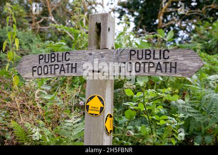 Panneau de sentier public indiquant quatre directions sur un poteau en bois abîmé.Deux pointeurs en bois sculpté, deux ronds-points imprimés jaune et noir Banque D'Images