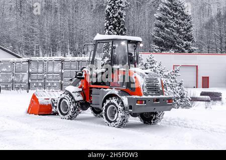 Homme sur un tracteur rouge avec chasse-neige déneigement pendant la chute de neige.Conditions météorologiques Blizzard.Entretien des rues en hiver.Rayon de champ peu profond Banque D'Images