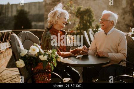 Un couple de personnes âgées en bonne santé tient la main dans le café en plein air lors d'une journée d'automne ensoleillée Banque D'Images