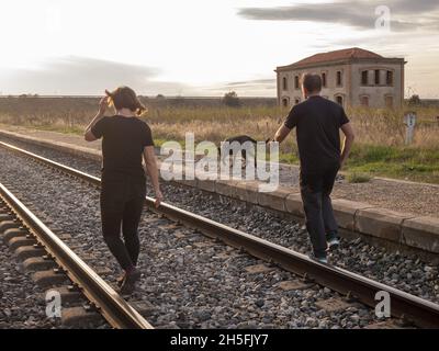 Couple adulte marchant avec leur chien sur un chemin de fer pendant le coucher du soleil Banque D'Images