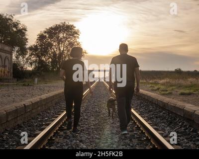 Couple adulte marchant avec leur chien sur un chemin de fer pendant le coucher du soleil Banque D'Images