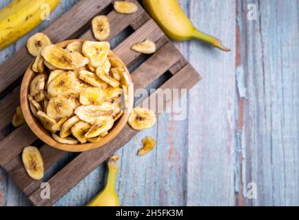 Vue de dessus des chips de banane biologique déshydratées sur le panneau en bois, décoré avec des bananes fraîches Banque D'Images