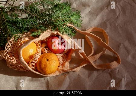 Noël écologique sans gaspillage.Pommes, tangerines, sac à ficelle avec branches d'épinette sur un fond de papier artisanal.Le concept d'une maison de vacances confortable Banque D'Images