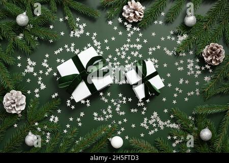 Composition de Noël avec boîtes-cadeaux, branches de sapin, cônes et étoiles confetti argentées.Heure de congé.Fond vert de Noël.Vue de dessus. Banque D'Images