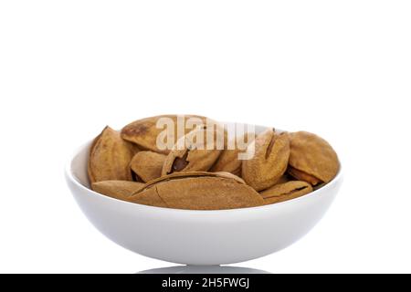 Amandes non pelées séchées dans une soucoupe en céramique blanche, en gros plan, isolées sur du blanc. Banque D'Images